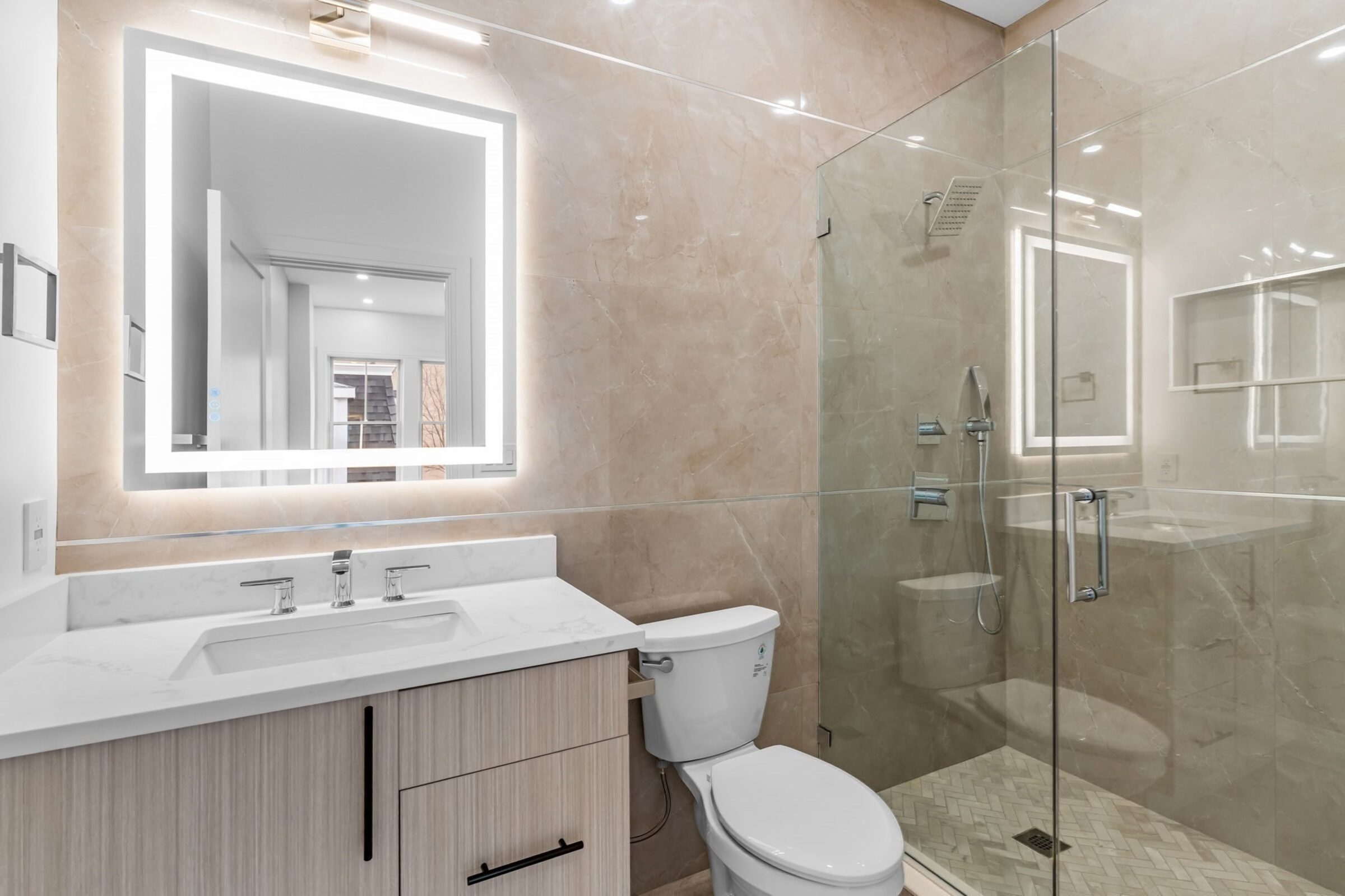 Primary bathroom with a backlit mirror and glass-enclosed shower.