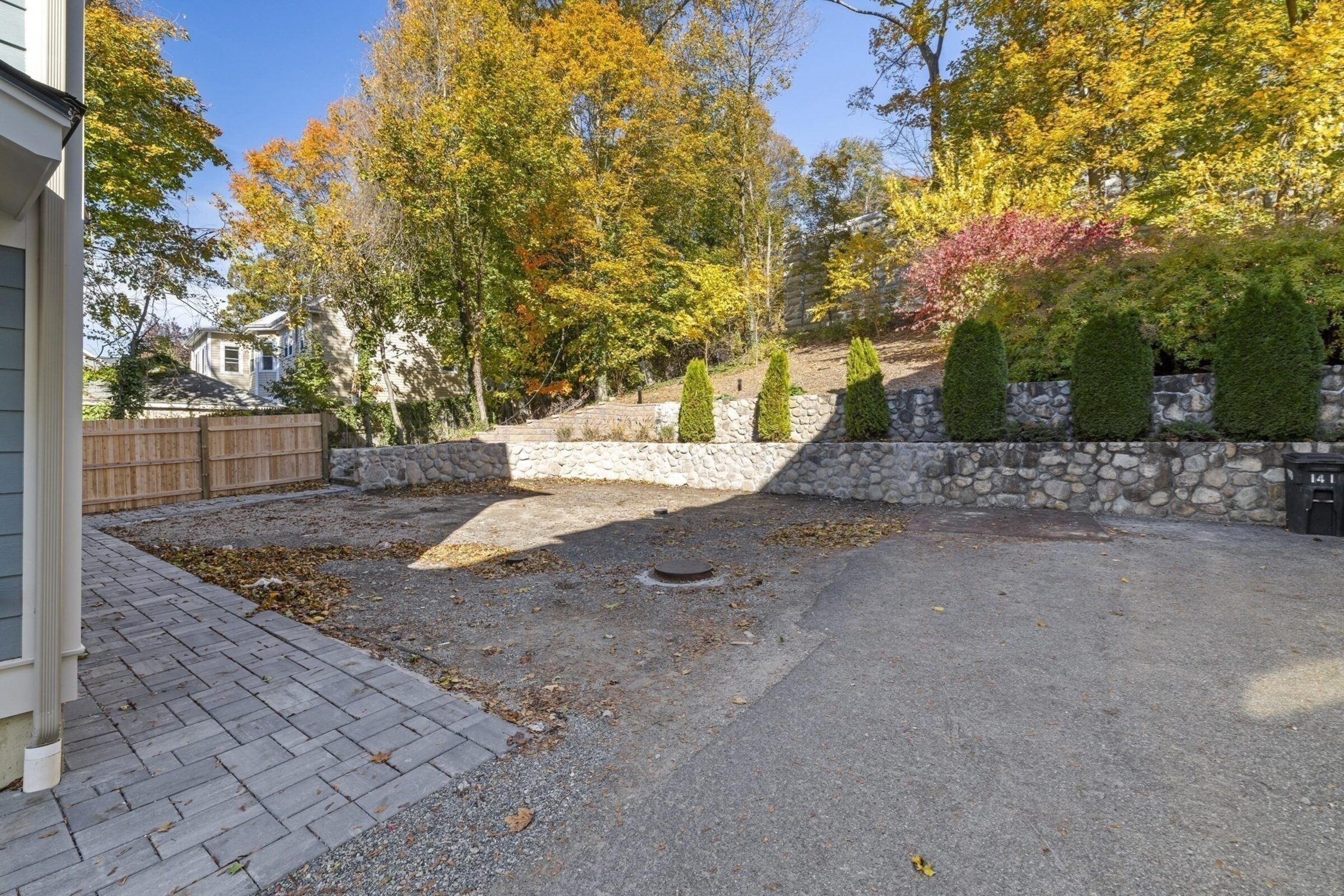 Rear yard with a stone retaining wall, framed by autumn trees.