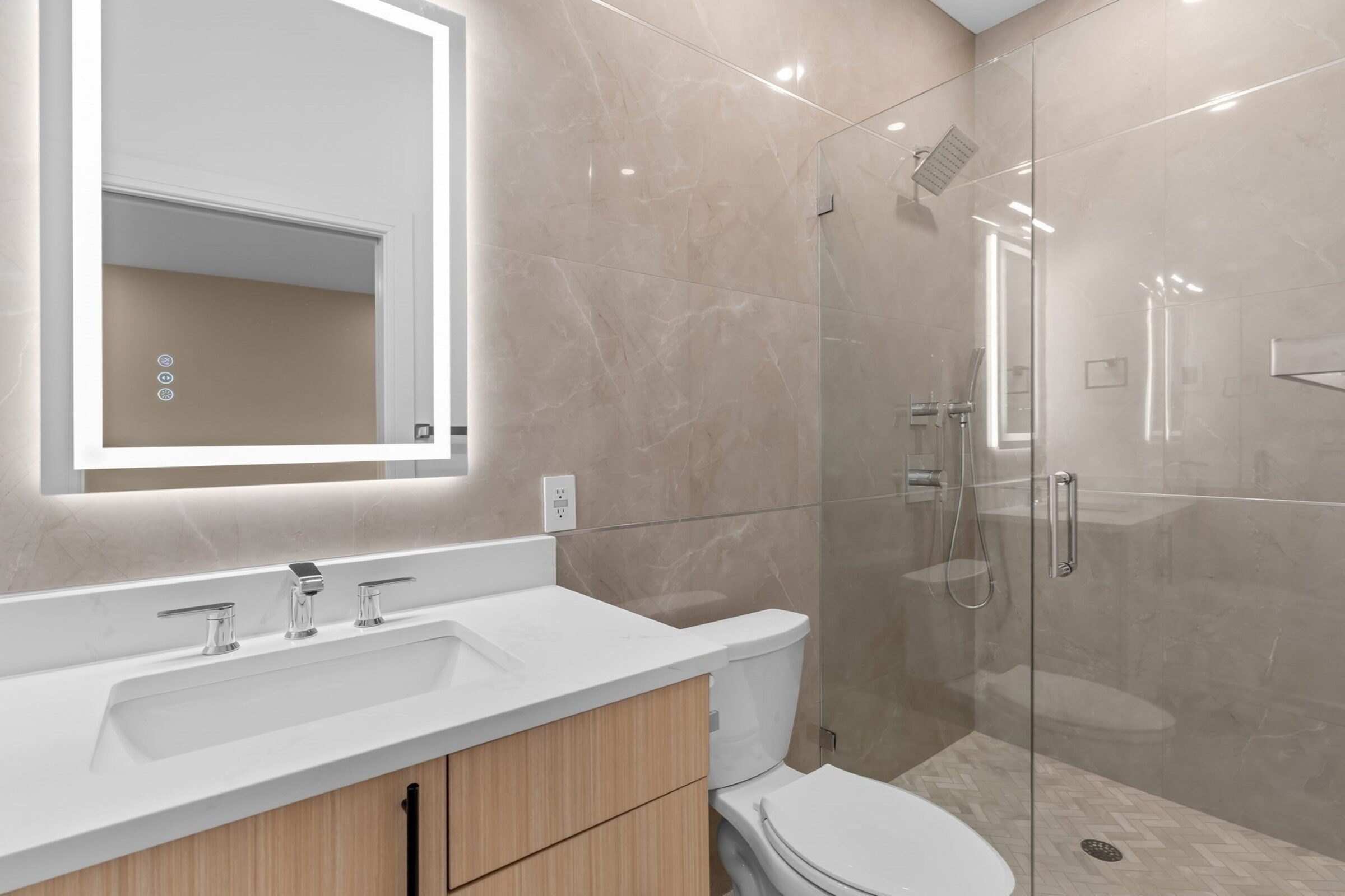 Bathroom with a backlit LED mirror, glass-enclosed shower, and marble finishes.